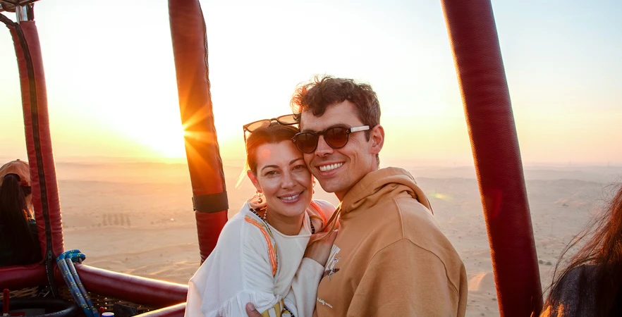 Couple enjoying sunrise during hot air balloon ride in Ras Al Khaimah desert.