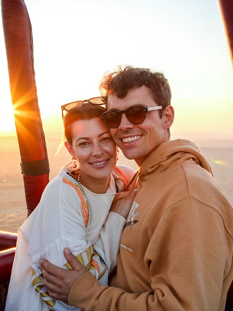 Couple enjoying sunrise during hot air balloon ride in Ras Al Khaimah desert.