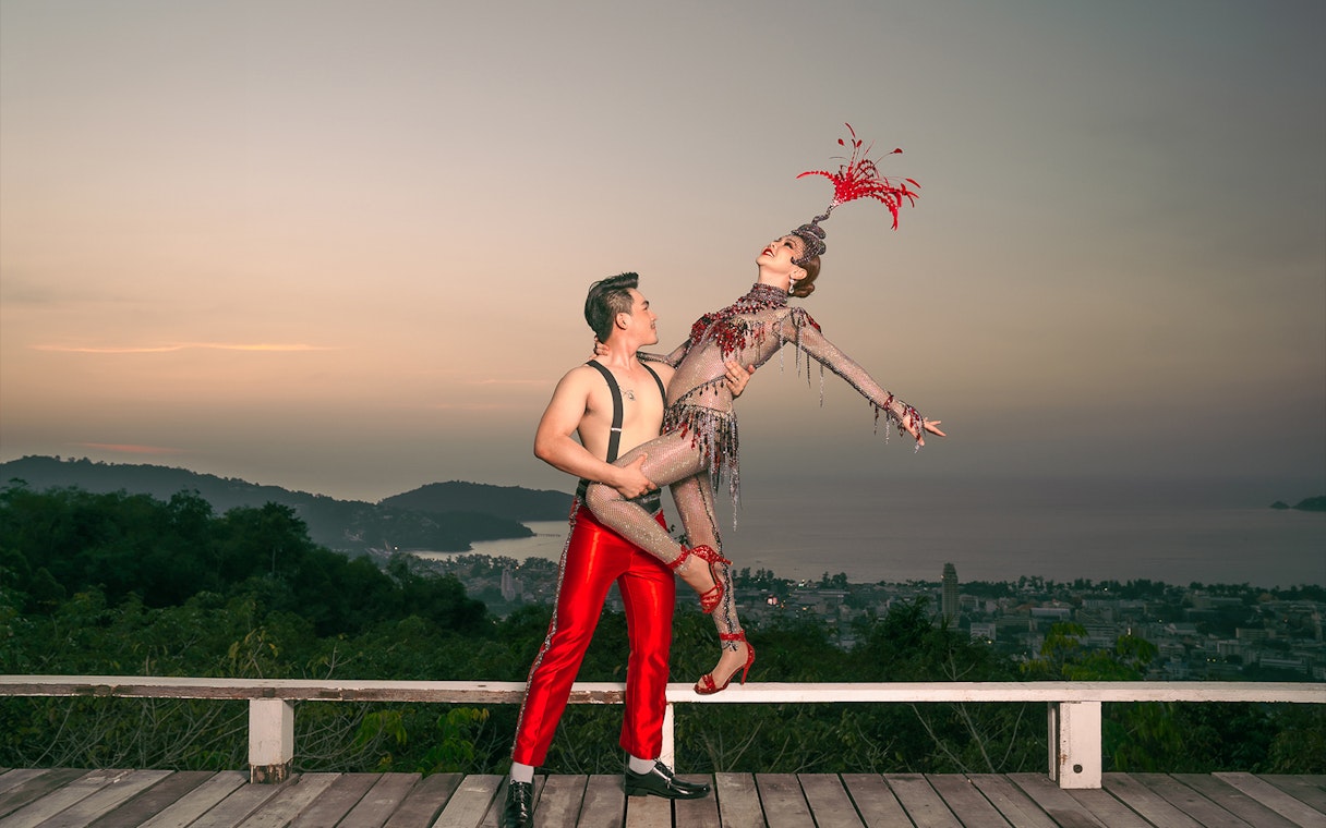 Performers in vibrant costumes at Simon Cabaret Show, Phuket, with scenic backdrop.