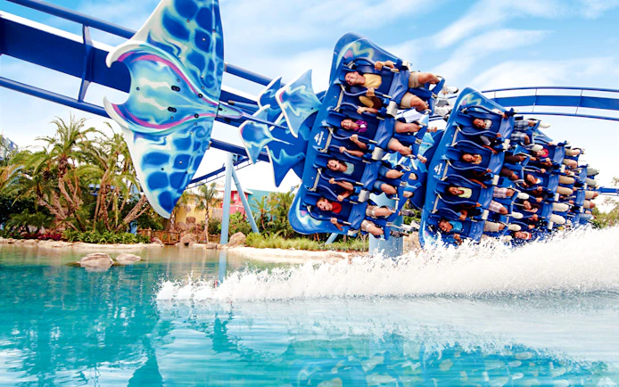 Riders on Manta roller coaster at SeaWorld Orlando skimming over water.