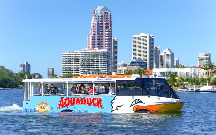 Aquaduck amphibious vehicle cruising on a river with city skyline in the background.