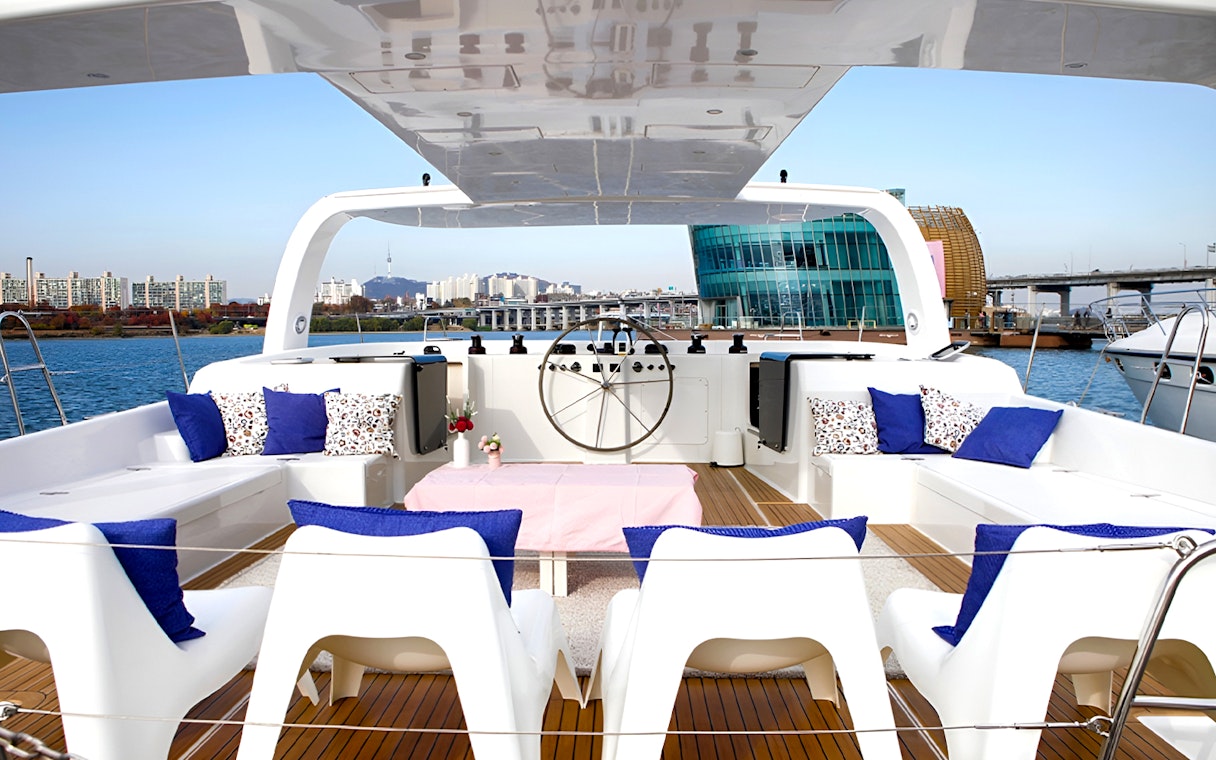 Yacht deck with seating area, blue cushions, and cityscape view in the background.