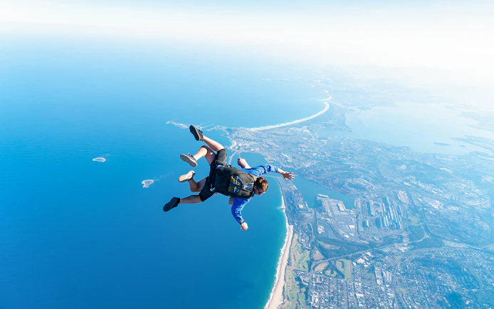 Skydivers tandem freefall over Wollongong coastline near Sydney.
