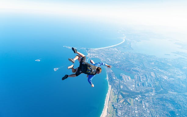 Skydivers tandem freefall over Wollongong coastline near Sydney.