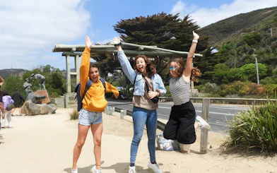 Tourists jumping at the Great Ocean Road entrance during Melbourne nature tour.