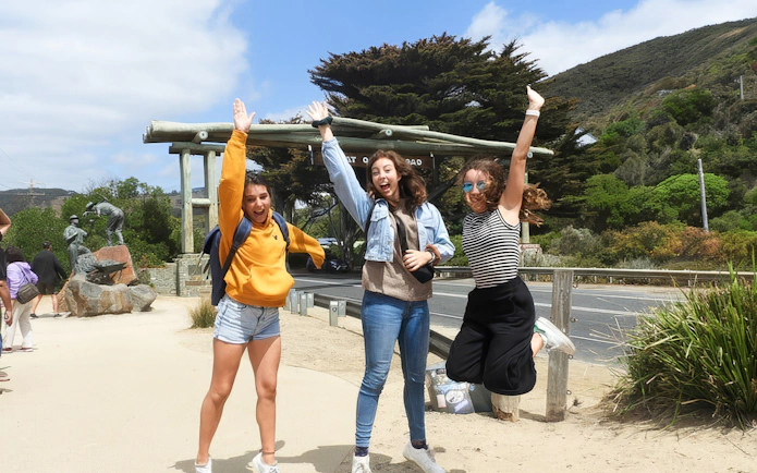 Tourists jumping at the Great Ocean Road entrance during Melbourne nature tour.