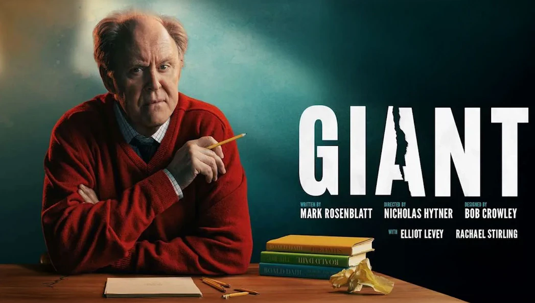 Man in red sweater holding pencil at desk with books, next to the word "Giant.