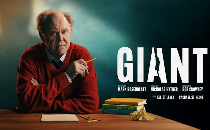 Man in red sweater holding pencil at desk with books, next to the word "Giant.
