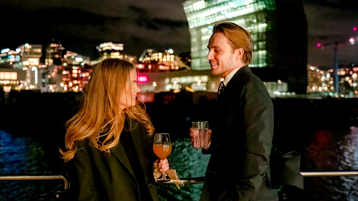 Couple enjoying drinks on an Oslo dinner cruise with city lights in the background.