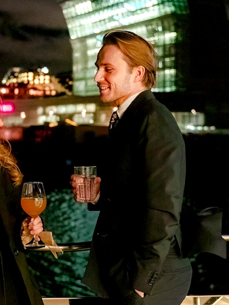 Couple enjoying drinks on an Oslo dinner cruise with city lights in the background.