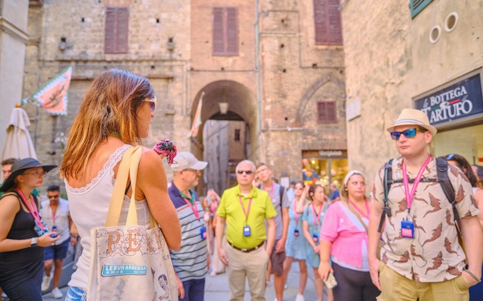 Tour guide speaking to tourists in a historic street during Pisa, Siena, and San Gimignano day trip.