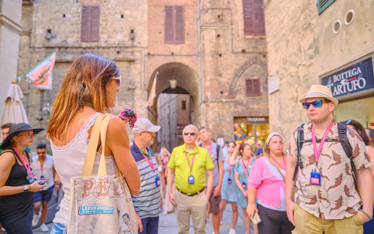 Tour guide speaking to tourists in a historic street during Pisa, Siena, and San Gimignano day trip.