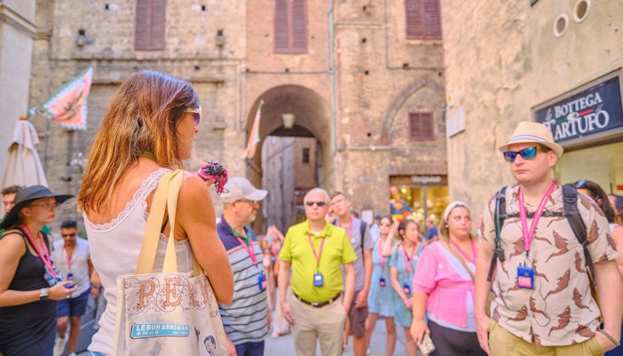 Tour guide speaking to tourists in a historic street during Pisa, Siena, and San Gimignano day trip.