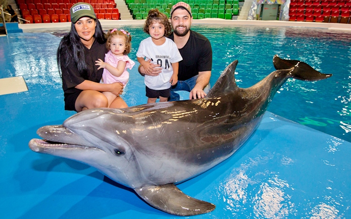 Tourists with children posing beside a dolphin at an aquarium.