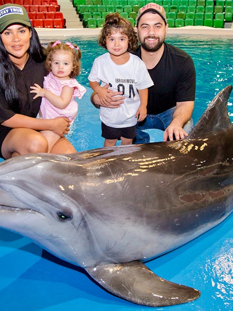 Tourists with children posing beside a dolphin at an aquarium.
