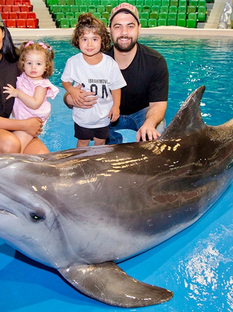 Tourists with children posing beside a dolphin at an aquarium.