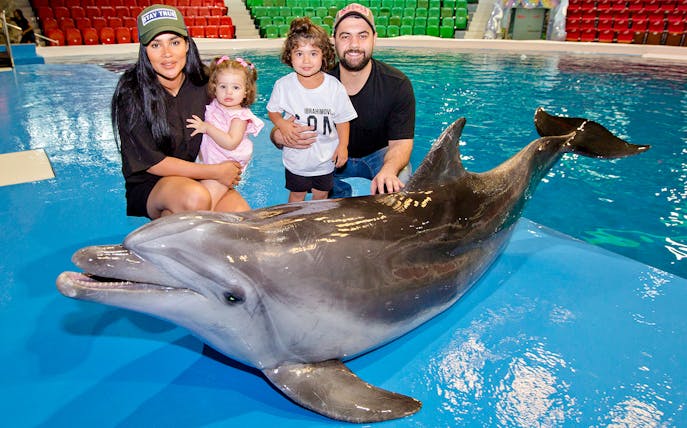 Tourists with children posing beside a dolphin at an aquarium.