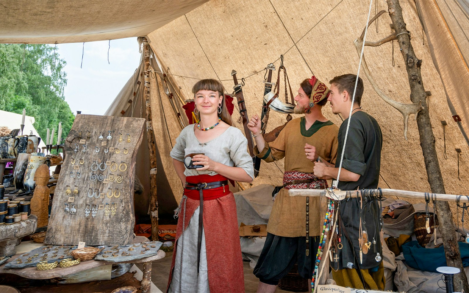 Viking reenactment with people in traditional clothing, jewelry display, and weapons in a tent.