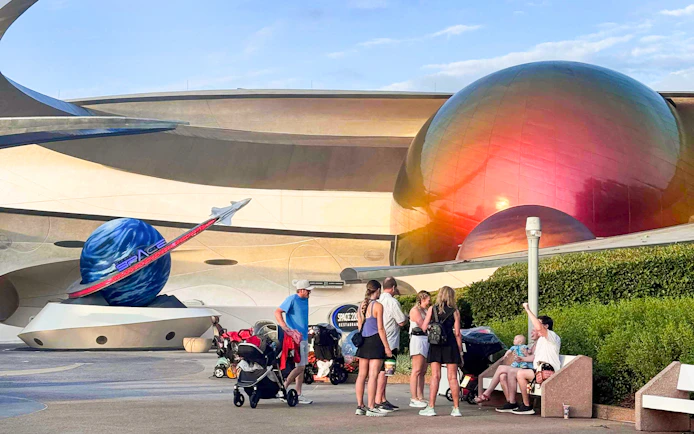 Visitors at Space Center, Walt Disney Resort Orlando, near futuristic architecture and space-themed decor.
