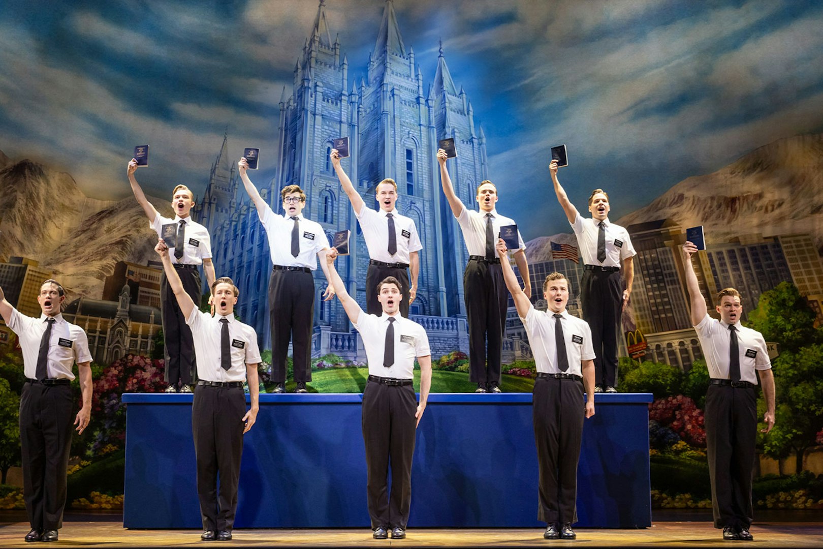 Cast performing The Book of Mormon on stage in Sydney with a backdrop of a temple.