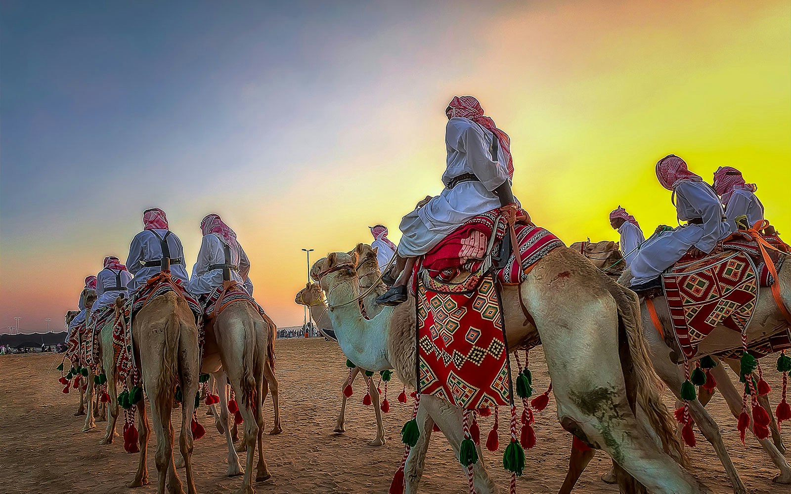 Camels with riders in traditional attire at sunset, Dubai desert safari.