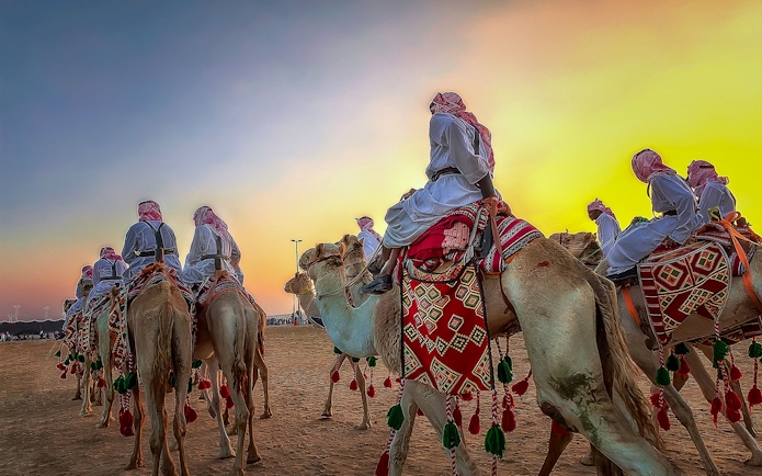 Camels with riders in traditional attire at sunset, Dubai desert safari.