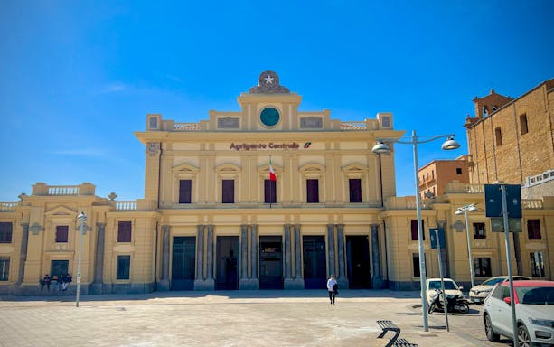 Agrigento Centrale Railway Station facade with Italian flag and clear sky.