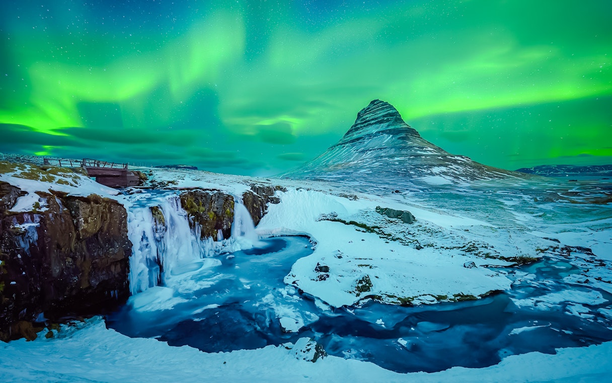Kirkjufell mountain with Northern Lights in Reykjavik, Iceland, over snowy landscape and waterfall.