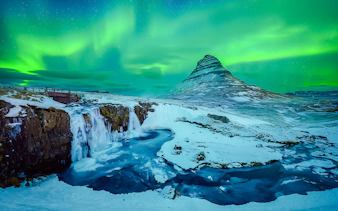 Kirkjufell mountain with Northern Lights in Reykjavik, Iceland, over snowy landscape and waterfall.