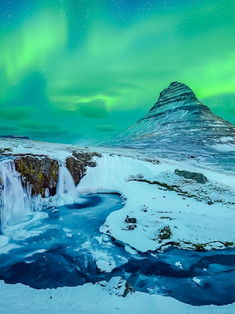 Kirkjufell mountain with Northern Lights in Reykjavik, Iceland, over snowy landscape and waterfall.