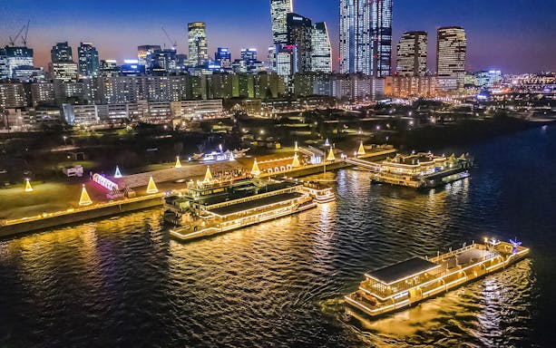 Han River night cruise with illuminated boats and Seoul skyline in the background.