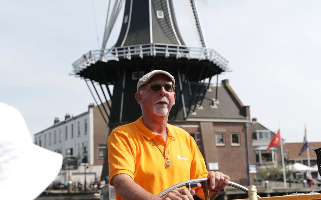 Skipper steering boat with windmill backdrop on Haarlem canal cruise.