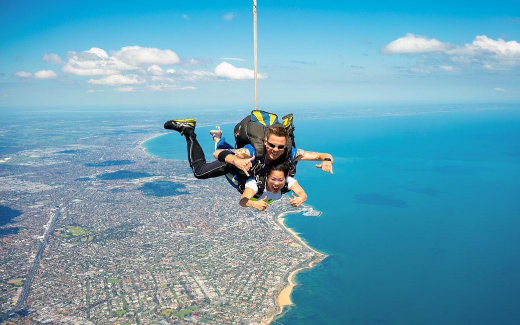 Tandem skydivers over St Kilda Beach, Melbourne with coastline view.