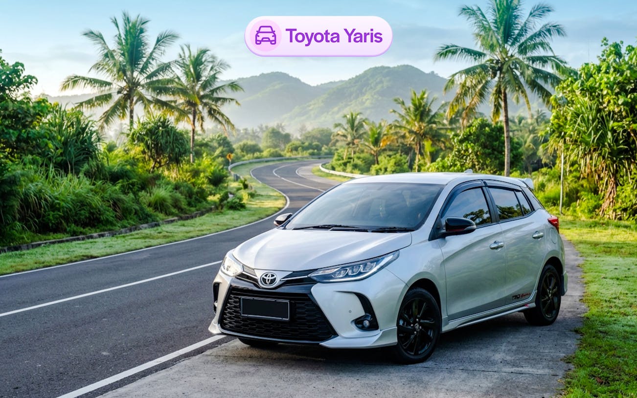 Toyota Yaris parked on a scenic road in Bali with palm trees and mountains.