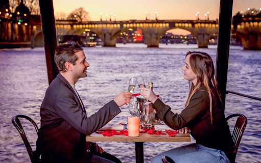 Couple toasting with champagne on a Seine River dinner cruise in Paris at sunset.