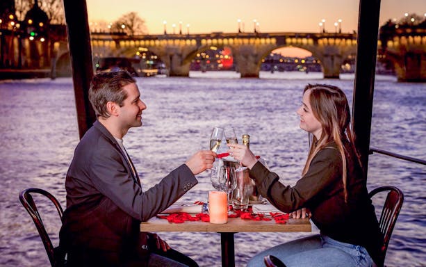 Couple toasting with champagne on a Seine River dinner cruise in Paris at sunset.