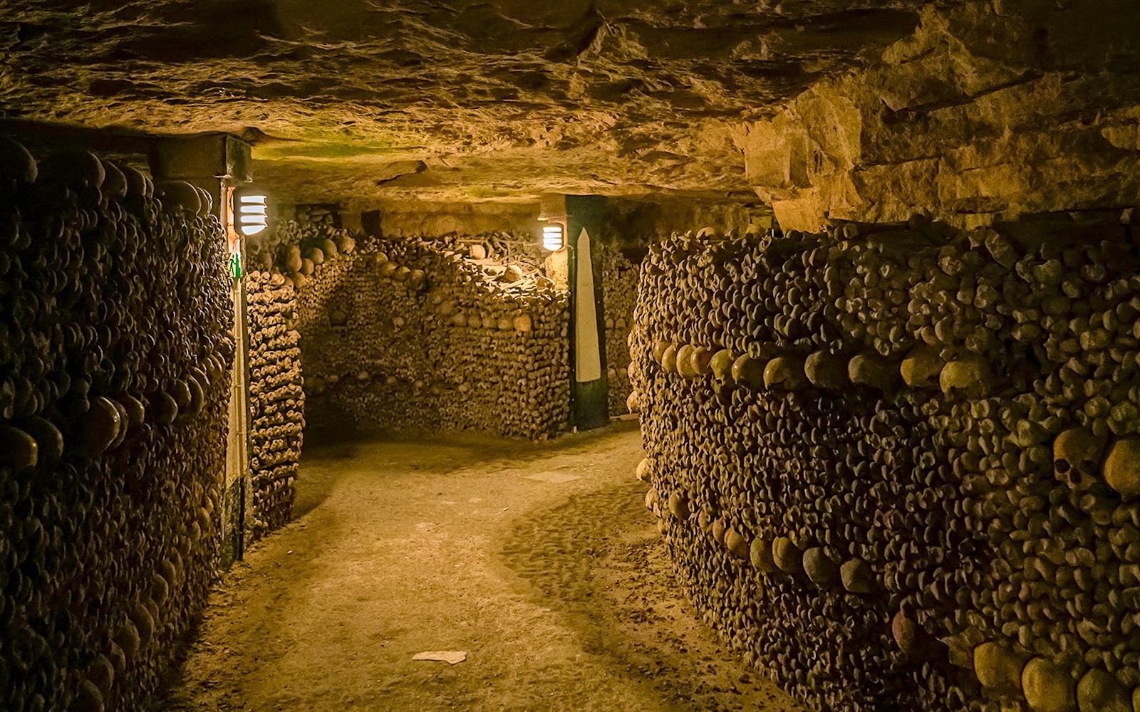 Paris Catacombs tunnel with walls of arranged skulls and bones.