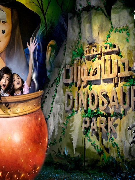 Visitors in a cauldron at Dubai Garden Glow's Dinosaur Park with dinosaur sculpture.