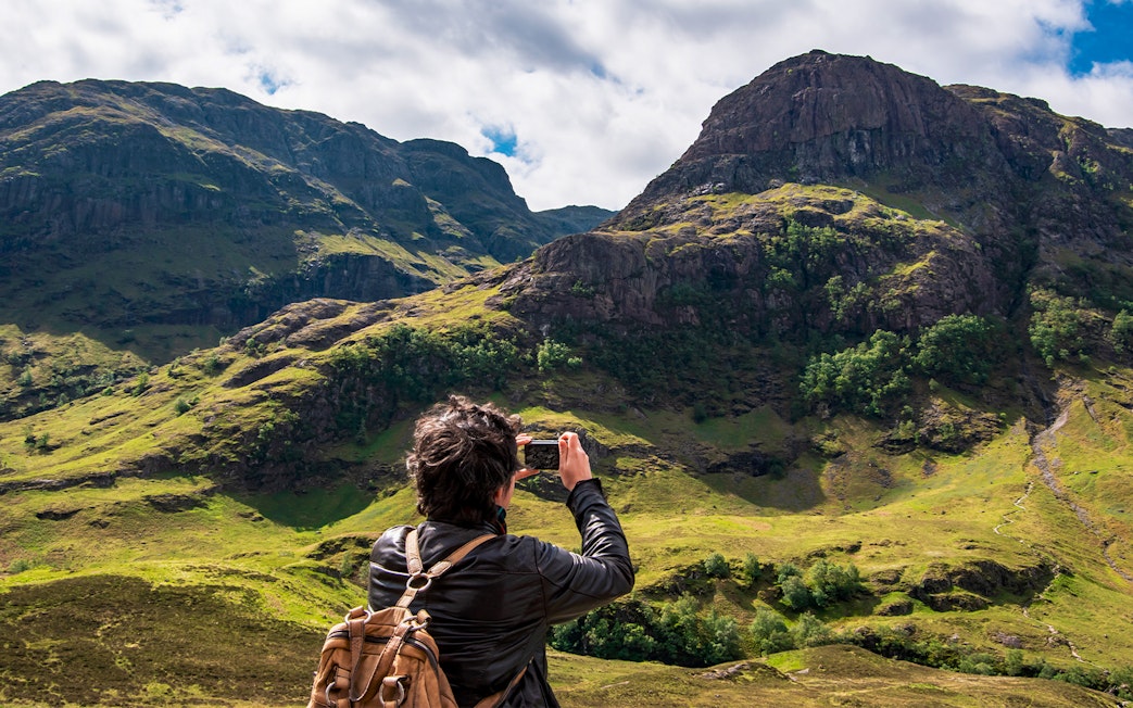 Tourist photographing the Three Sisters of Glencoe, Scotland.