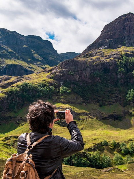 Tourist photographing the Three Sisters of Glencoe, Scotland.
