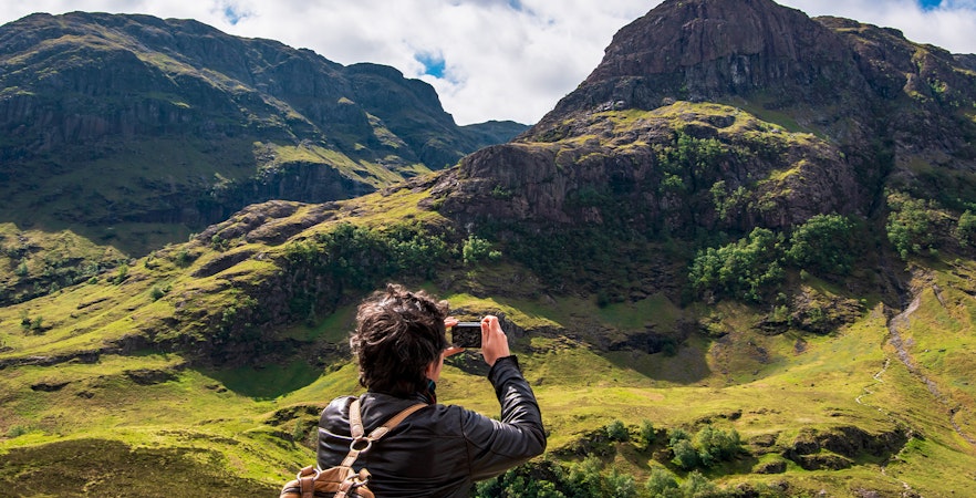 Tourist photographing the Three Sisters of Glencoe, Scotland.