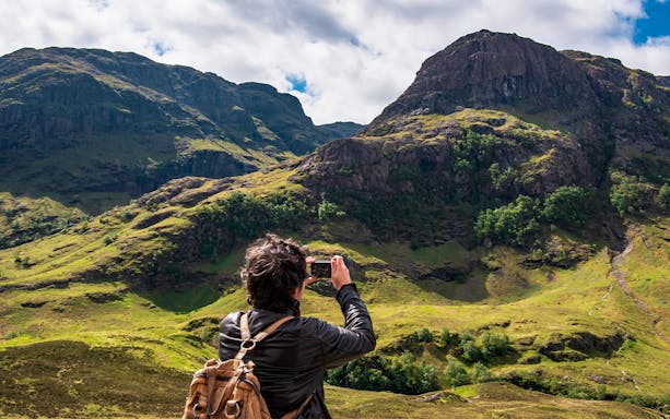 Tourist photographing the Three Sisters of Glencoe, Scotland.