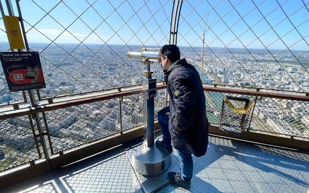 Person using telescope on Eiffel Tower observation deck, Paris, France.