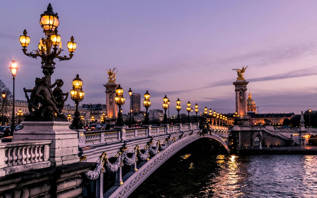 Illuminated Pont Alexandre III bridge in Paris at dusk.