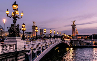 Illuminated Pont Alexandre III bridge in Paris at dusk.