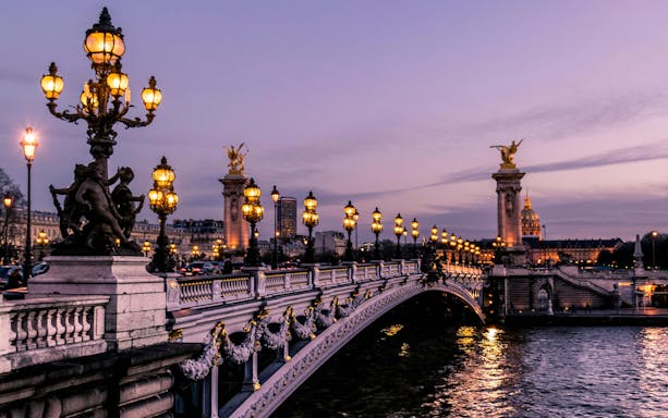 Illuminated Pont Alexandre III bridge in Paris at dusk.