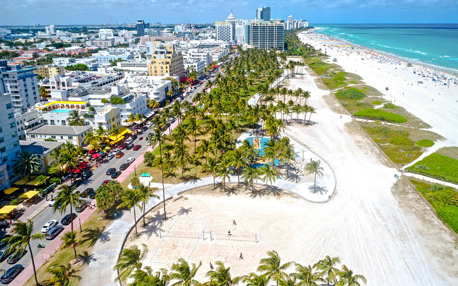 People enjoying a sunny day at Lummus Park, Miami Beach, with palm trees and ocean in the background.