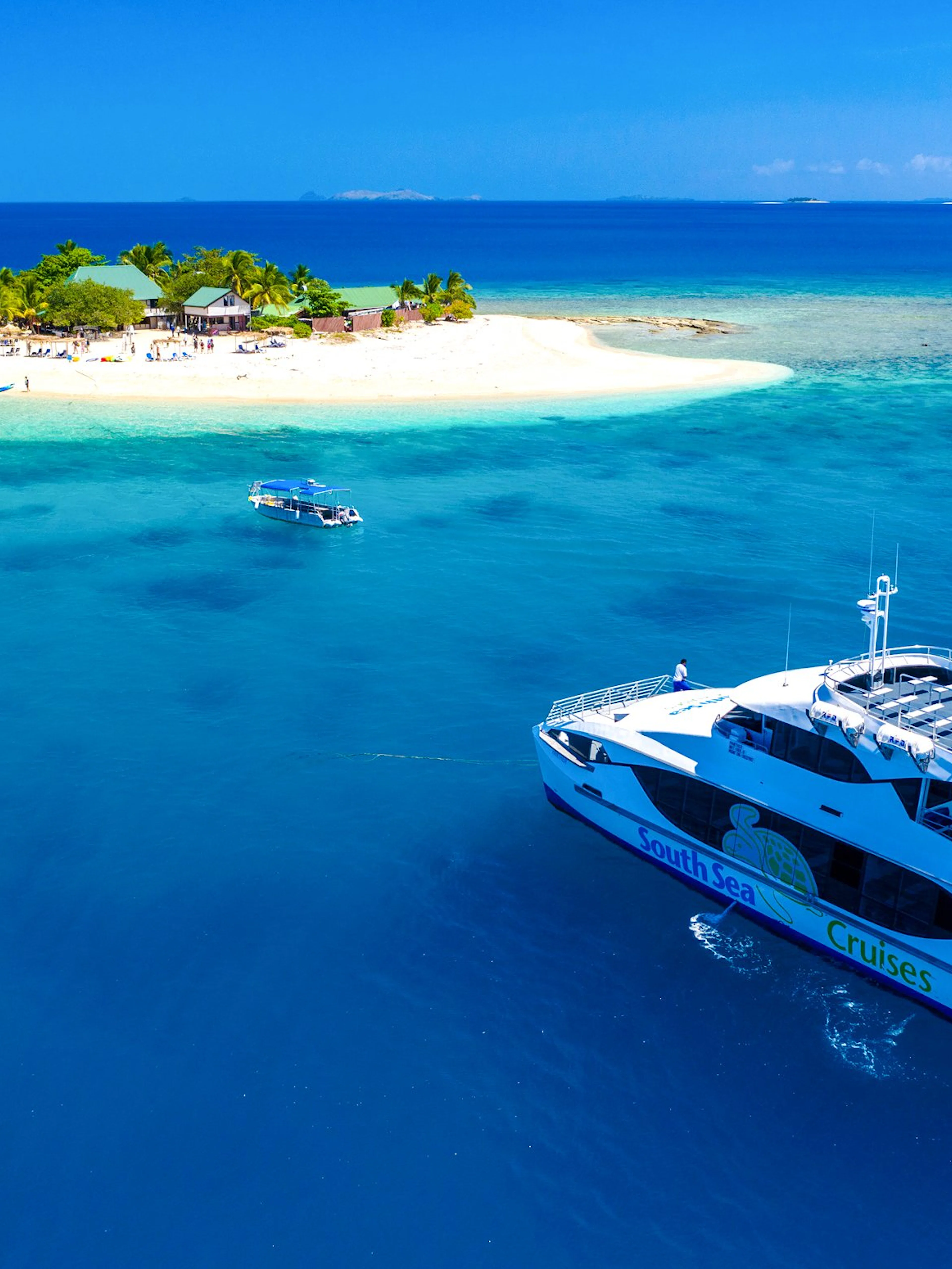 Cruise ship near South Sea Island, Fiji, with beach and palm trees in view.
