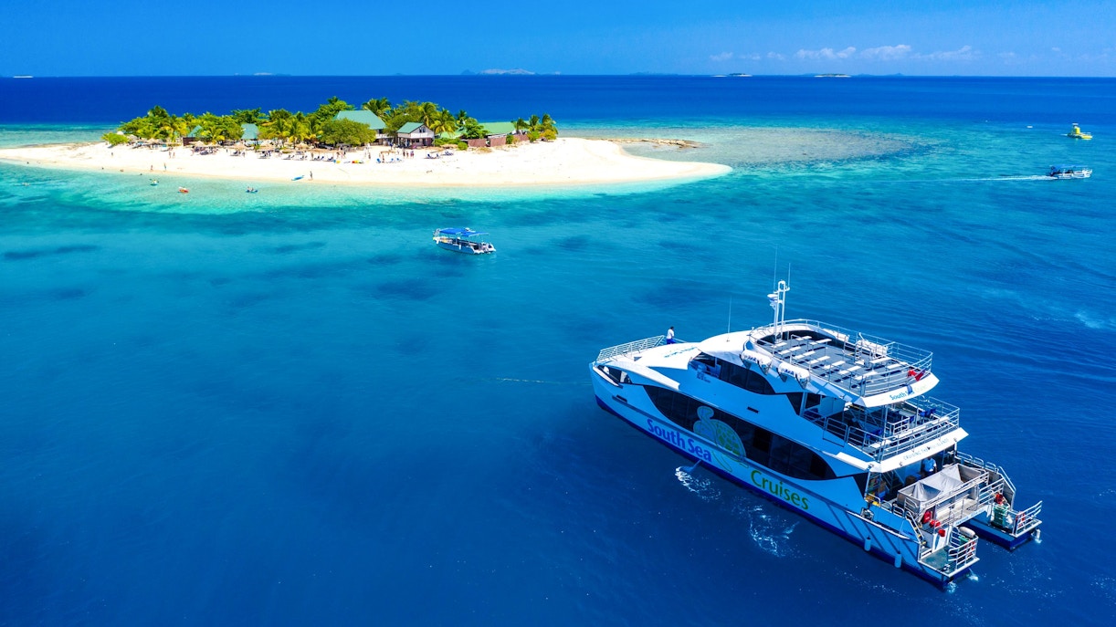 Cruise ship near South Sea Island, Fiji, with beach and palm trees in view.