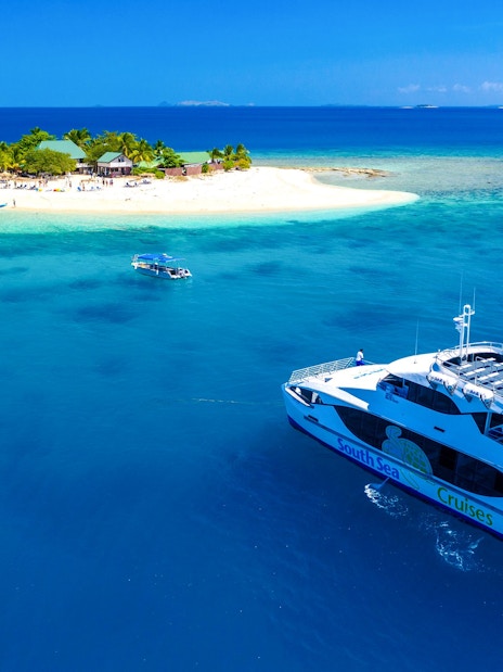 Cruise ship near South Sea Island, Fiji, with beach and palm trees in view.